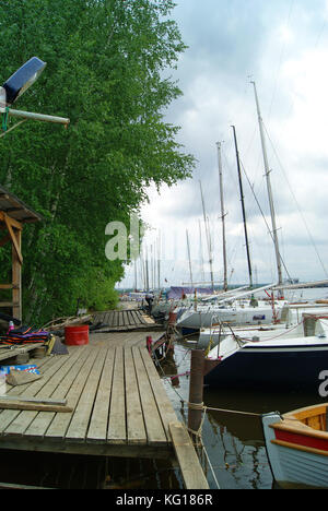 Ausgehende hölzernen Pier entlang einer bewaldeten Ufer und eine Reihe von Segelyachten günstig entlang es Stockfoto