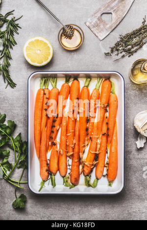Gebratene Möhren mit Thymian, Knoblauch, Zitrone und Honig auf Backen versuchen, kochen Vorbereitung. Gesundes Wurzelgemüse Konzept Stockfoto