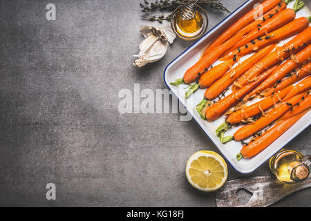 Gebratene baby überstieg Karotten auf Backblech mit Thymian, Honig, Knoblauch und Zitrone auf grauem Beton Hintergrund, Ansicht von oben, Grenze. Gesundes Wurzelgemüse Stockfoto