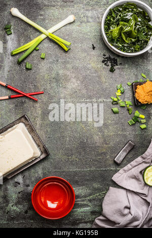 Zutaten zum Kochen für japanische Miso Suppe: wakame Algen, silken Tofu, Frühlingszwiebeln und Miso einfügen im Alter von Hintergrund, Ansicht von oben, Rahmen Stockfoto