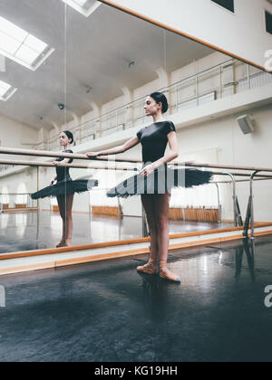 Ballerina in Schwarz tutu und Pointe erstreckt sich auf Barre im Ballett Fitnessraum. Frau, die in der Nähe von Bar und Spiegel, die Vorbereitung auf die Leistung. Stockfoto