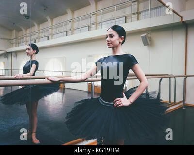 Ballerina in Schwarz tutu und Pointe erstreckt sich auf Barre im Ballett Fitnessraum. Frau, die in der Nähe von Bar und Spiegel, die Vorbereitung auf die Leistung. Stockfoto