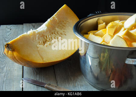 Kürbis Keil, ein Topf mit Kürbis Bits und ein Messer auf einem Holztisch Stockfoto