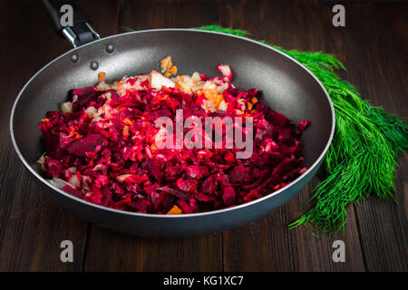 Karotten, Rüben und Zwiebeln in einer Pfanne, um Dill, auf braunem Holz- Hintergrund. Zutaten für borsch Stockfoto