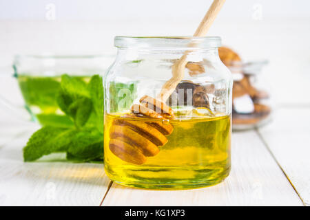 Ein Honigtopf mit einem Löffel auf einem weißen Tisch. Im Hintergrund, Minze Stockfoto