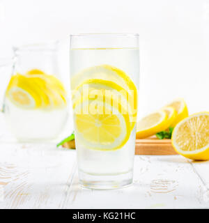 Ein Becherglas und einen Krug kalten Limonade auf einem weißen Hintergrund Holz umgeben von Zitronen Stockfoto