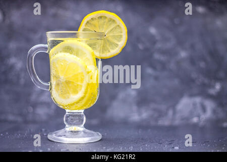 Hausgemachte Limonade in ein Glas mit einem Handgriff über ein grauer Beton Hintergrund. Wasser mit Zitronenscheiben auf einem dunklen Hintergrund. Stockfoto