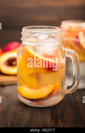 Mason jar Glas hausgemachten Pfirsich Eiswasser auf einem rustikalen Holzmöbeln Hintergrund. Stockfoto