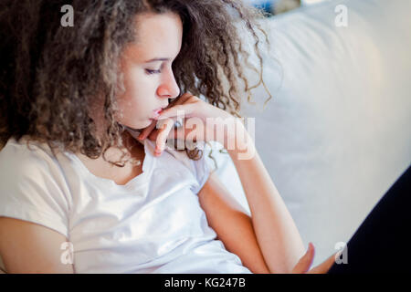 Portrait von lockigem Haar jugendlich Mädchen sitzt auf einem Sofa Stockfoto