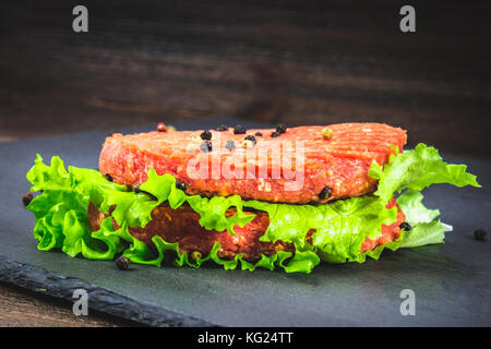 Raw Burger mit Salat auf einem grauen Hintergrund Stockfoto