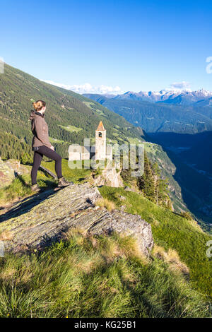 Die Frau schaut auf die alte Kirche auf den Bergen, die San Romerio Alp, Brusio, den Kanton Graubünden, das Poschiavo-Tal, Schweiz, Europa Stockfoto