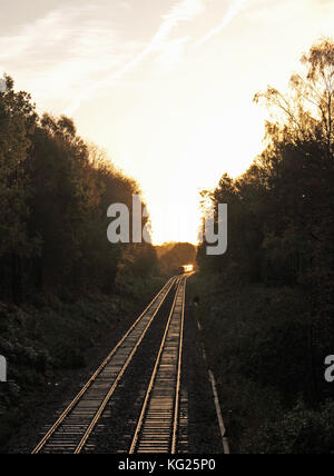 Am frühen Morgen fährt ein Zug entlang der Gleise und die Schlafenden werden von der aufgehenden Sonne beleuchtet, da er um eine Kurve verschwindet. Stockfoto