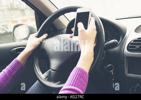 Telefon in den Händen von Frauen. Mädchen in einem Auto hinter dem Lenkrad Stockfoto