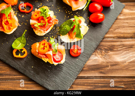 Canapes Vorspeise mit Schinken, Paprika, Tomaten und grünen Spinat und Rucola Blätter, gesund Crostini oder Bruschetta italienische Vorspeise Stockfoto