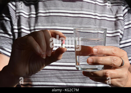 Gesundheitswesen & Arzneimittel. Frau mit einem Gel Kapsel und ein Glas Wasser. Mittelteil. Stockfoto