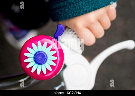 Child's Hand am Lenker eines Fahrrades. Rosa Bell mit einer Blume dekoriert. Rimrose Valley Park, Sefton, Liverpool, Merseyside. Stockfoto