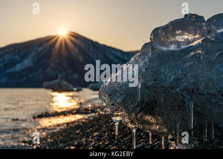 Bunte Winter Blick auf das Meer, die Berge, die Sonne, das Eis auf dem Ufer und die Sonne auf dem Wasser bei Sonnenuntergang Stockfoto