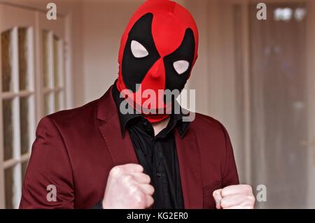 Mann in deadpool Maske und Burgund Anzug für Halloween Festlichkeiten posing Stockfoto