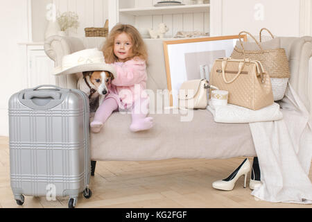 Ein kleines Mädchen mit Koffer und ein Hund im Innenraum Stockfoto