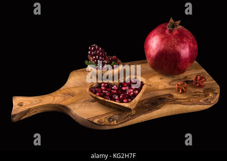 Ganze rote reife Granatapfel, Scheibe von Granatapfel und seinen Samen auf natürliche Holz Schneidebrett angeordnet. Stockfoto