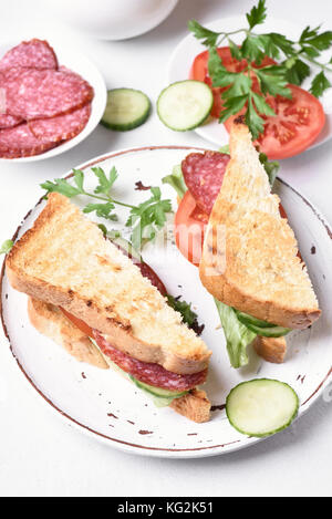 Club Sandwiches mit Salami, Tomaten, Gurken und Kopfsalat am weißen Stein Hintergrund Stockfoto
