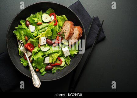 Grüner Salat mit Käse und frisches Gemüse auf einem schwarzen Hintergrund. griechischen Salat. Stockfoto