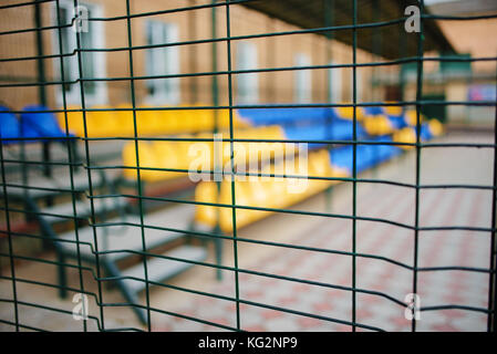Nahaufnahme metallic net-förmige Zaun aus Draht auf dem Hintergrund der leeren blauen und gelben Sportsitze des Grand stand. Stockfoto