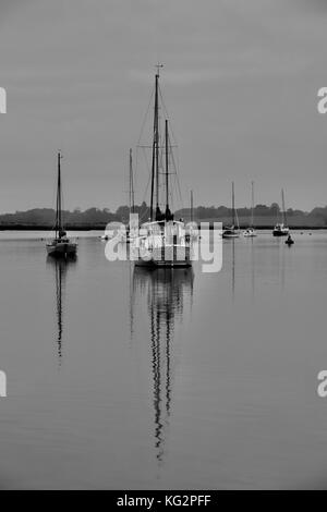 Schwarz-Weiß-Porträt des „Odin“-Segelbootes und dessen Spiegelung, vertäut im Fluss Deben am Waldringfield. Stockfoto