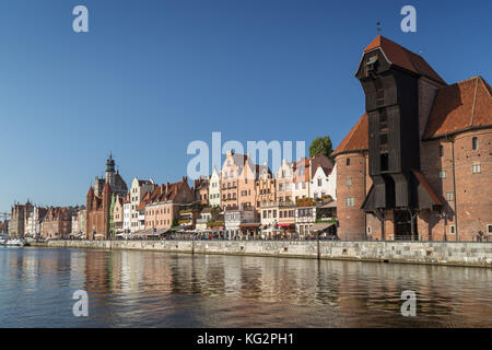 Blick auf den Kran und andere alte Gebäude entlang der langen Brücke Waterfront und ihre Reflexionen über die Mottlau in der Innenstadt von Danzig. Stockfoto