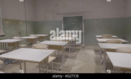 Leeres Klassenzimmer mit Holzschreibtischen, weißen und grünen Kreidebrettern in der Schule. Leerer Schulungsraum. Verlassener Schulraum mit Schreibtischen und Tafel Stockfoto