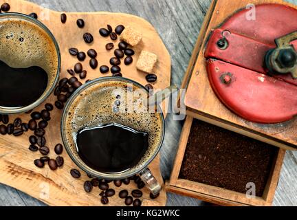 Zwei Tassen Kaffee, Kaffeebohnen, Braune Klumpen Zucker und Kaffee Schleifer auf Holz- Hintergrund. Stockfoto