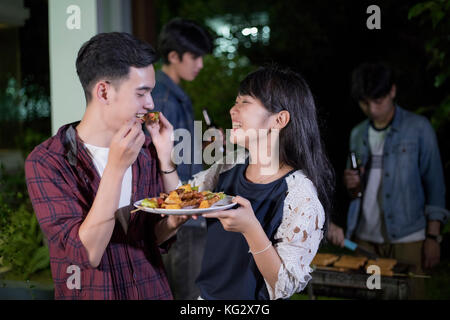 Asiatisches junges Paar beim romantischen Dinner und eine Gruppe von Freunden in Außenbereich Garten Grill Lachen mit alkoholfreien Bier Getränke bei Nacht Stockfoto