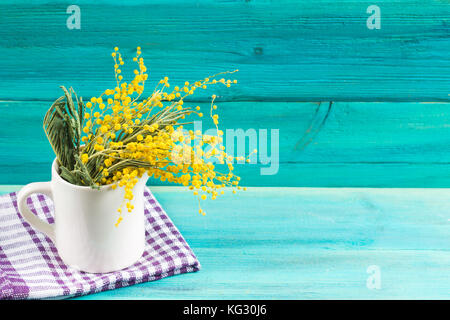 Gelb Frühling Blumen von Mimosa in eine weiße Tasse auf einem blauen Hintergrund aus Holz Stockfoto