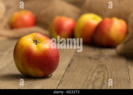 Nahaufnahme einer rot und gelb Apple auf einem Holzbrett mit vier mehr Äpfel und Hessischen im Hintergrund Stockfoto