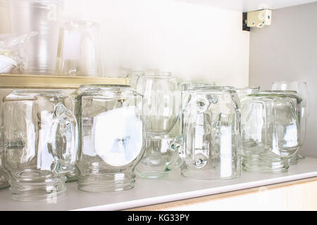Verschiedene Gläser in einem weißen Schrank auf dem Regal. Banken, Krüge, Gläser, Becher. Stockfoto