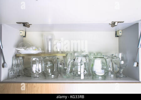 Verschiedene Gläser in einem weißen Schrank auf dem Regal. Banken, Krüge, Gläser, Becher. Stockfoto