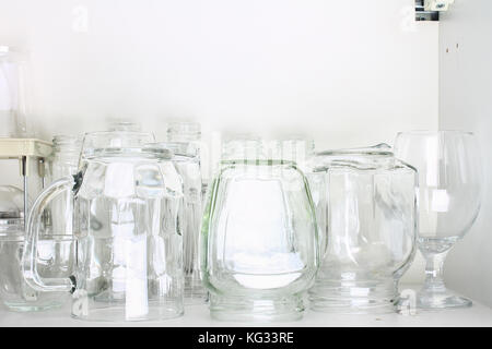 Verschiedene Gläser in einem weißen Schrank auf dem Regal. Banken, Krüge, Gläser, Becher. Stockfoto