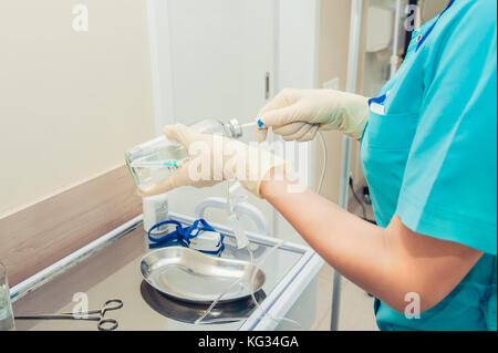 Arzt Frau in sterile Handschuhe Vorbereitung Katheter für Tropfenzähler. Dropper in eine Vene in der Nähe - auf dem Hintergrund der Chirurgischen funktionsfähig. selektive Fokus, Platz für Text Stockfoto