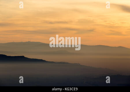 Ein Tal von Nebel bei Sonnenuntergang, gefüllt mit verschiedenen Schichten aus Hügeln und Bergen, und warmen Farben in den Himmel Stockfoto