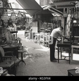 1950s, historisch, ein Stallholder, der Möbel in einem Durchgang an einem der berühmten Pariser Puces putzt, Flohmärkte, die alles von antiken Möbeln bis zu Vintage Bric-a-brac, Paris, Frankreich, zum Verkauf haben. Stockfoto