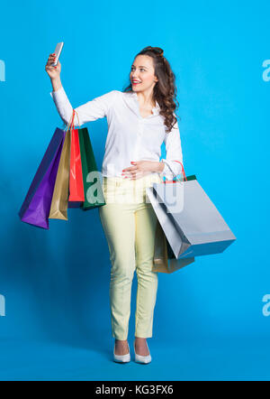 In voller Länge Porträt der jungen Frau mit vielen bunten Einkaufstaschen auf blauem Hintergrund. Stockfoto