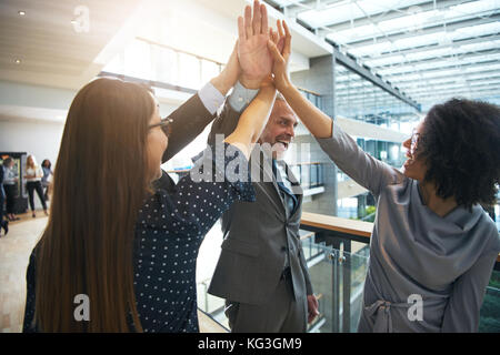 Vielfältige Gruppe von lächelnden Geschäftsleute hohe fiving einander beim zusammen in einem Korridor von einem modernen Bürogebäude stehend Stockfoto