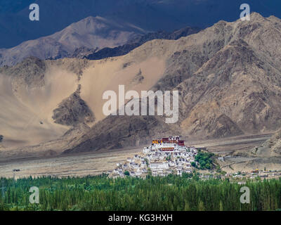 Buddhistische Stadt tiksi Kloster vor dem Hintergrund der riesigen Bergen von Braun und Beige, im Vordergrund ein Streifen von grünen Bäumen, Ladakh, Nort Stockfoto