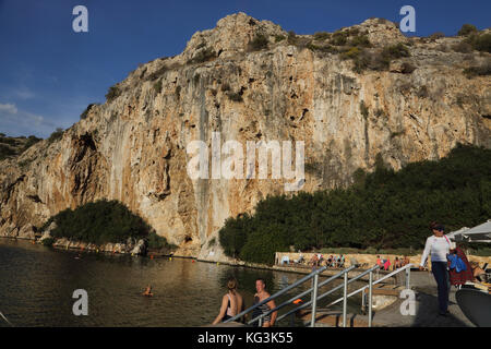 Vouliagmeni Athen Griechenland Touristen, die im Vouliagmeni-See schwimmen, ein Naturbad - war einst eine Höhle, aber das Höhlendach fiel durch Erosion durch die hohe Temperatur des fließenden Wassers ein. Stockfoto