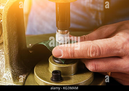 Eine Nahaufnahme eines Kürschner klappen Black Metal Tasten auf einem braunen Leder Gürtel auf einem alten Hand nietmaschine Maschine Stockfoto