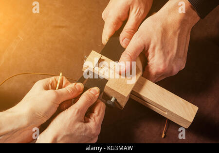 Eine Nahaufnahme eines Kürschner und sein Assistent schneidet ein Stück Leder einen schwarzen Gürtel auf speziellen Maschinen auf einem braunen Tabelle, Ansicht von oben zu erstellen Stockfoto