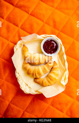 Eine Nahaufnahme von drei frische Croissants mit Schokoladenfüllung und Erdbeermarmelade mit einer Platte liegen auf einer Serviette in einem Weidenkorb auf eine Bettdecke für die Pause Stockfoto