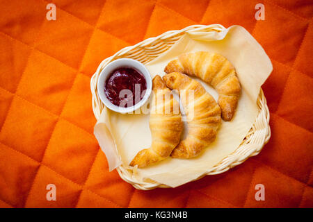 Eine Nahaufnahme von drei frische Croissants mit Schokoladenfüllung und Erdbeermarmelade mit einer Platte liegen auf einer Serviette in einem Weidenkorb auf eine Bettdecke für die Pause Stockfoto