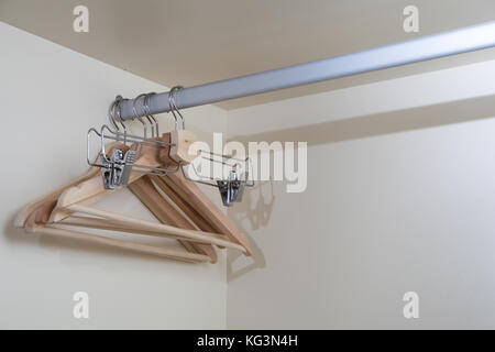 Eine Nahaufnahme der hölzernen Leer beige Kleiderbügel für Aufbewahrung von Kleidung und lange Hosen hängen in einer Reihe auf einem mettalical Regal in einem beige Gehäuse Stockfoto