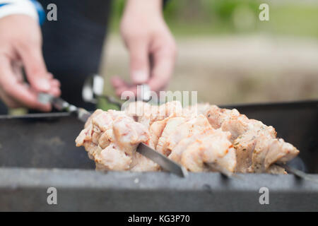 Rohes Fleisch am Spieß im Laufe der Braten. männliche Hände Schliessen gedrückt halten Spieße. Spieße mit Fleisch liegen auf einem brazier Stockfoto